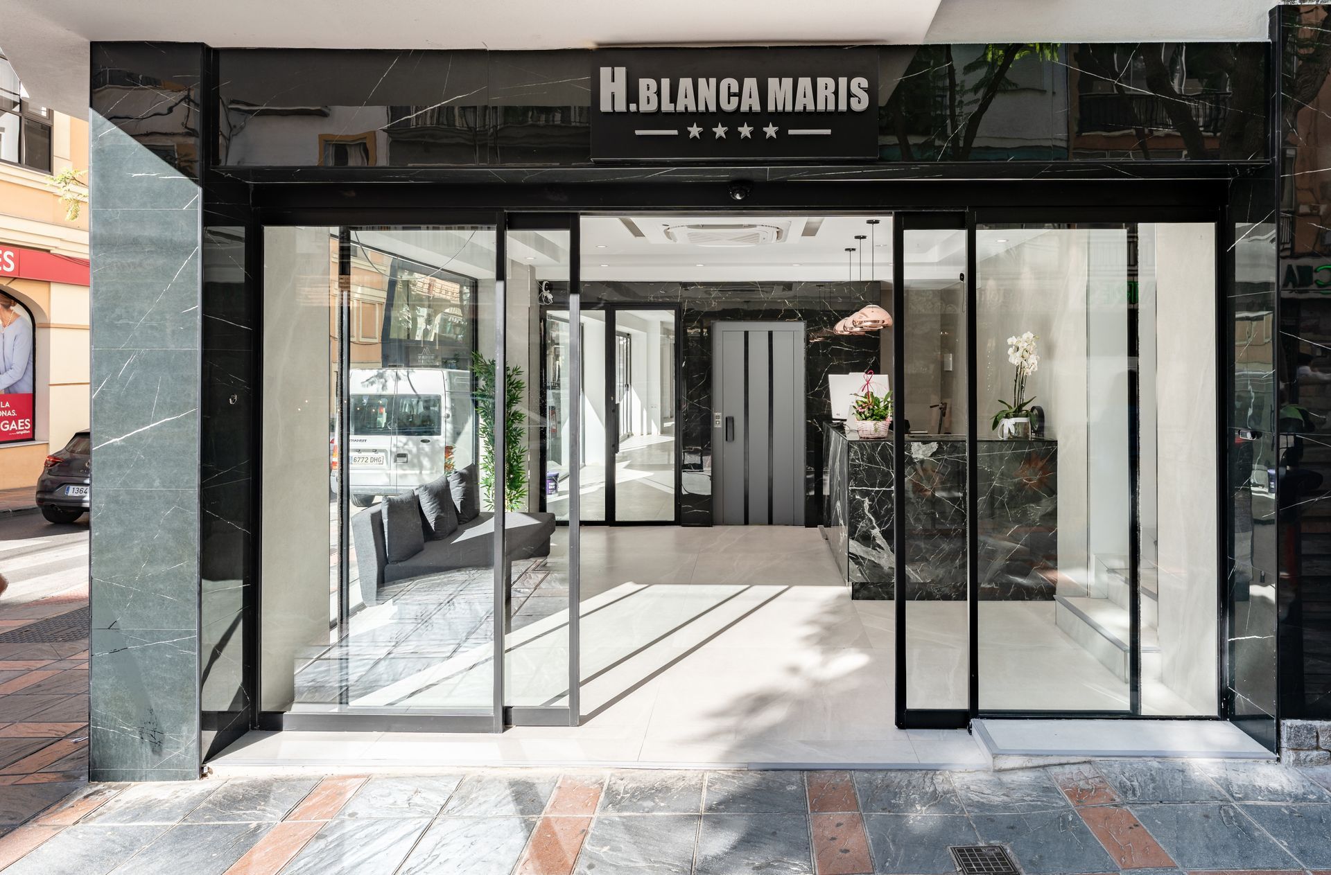 Entrada del Hotel Blanca Maris, diseño moderno con puertas corredizas de vidrio, detalles de mármol y vestíbulo abierto.