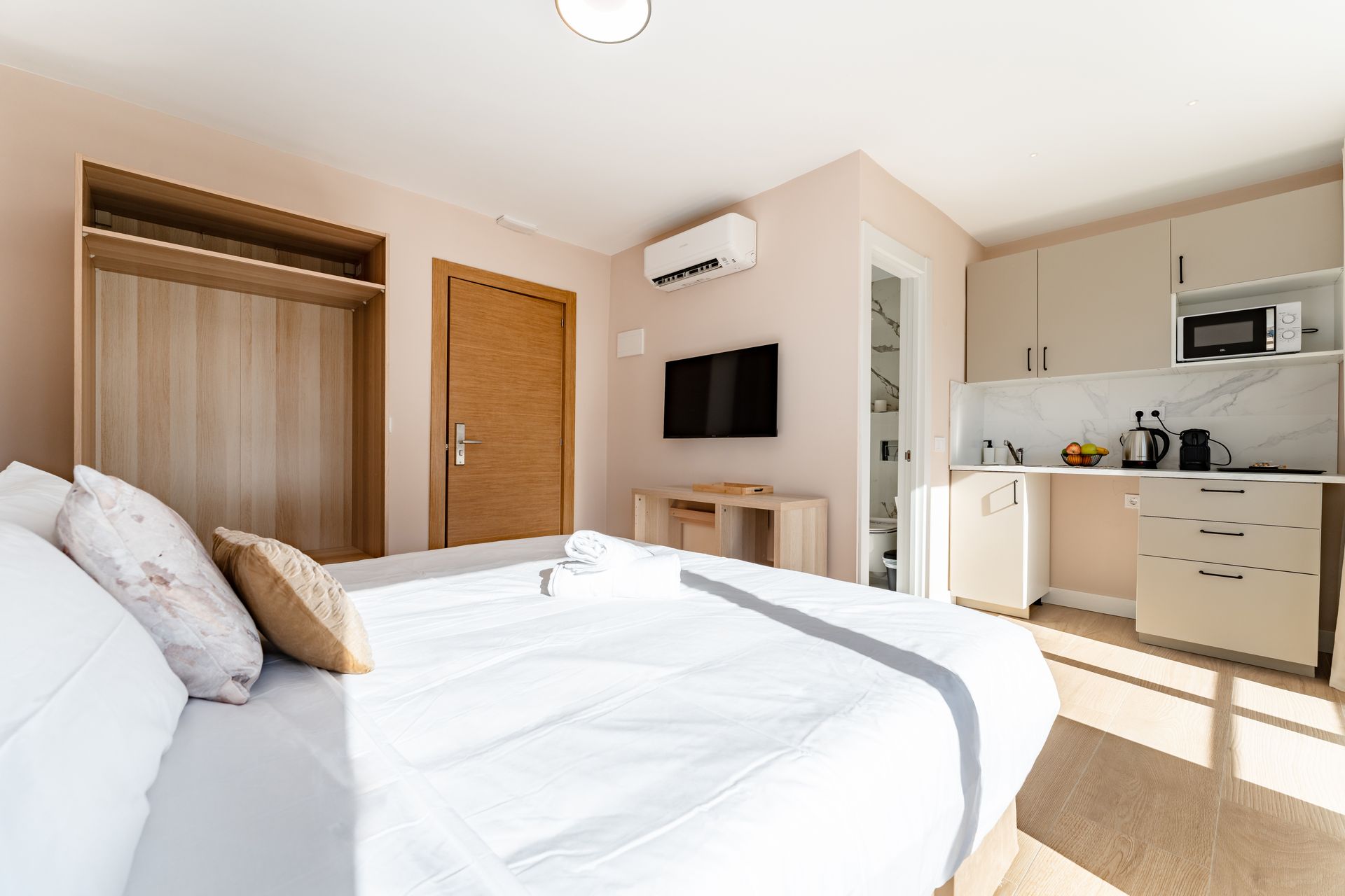 Dormitorio con cama, armario, TV, cocina americana y puerta abierta al baño.