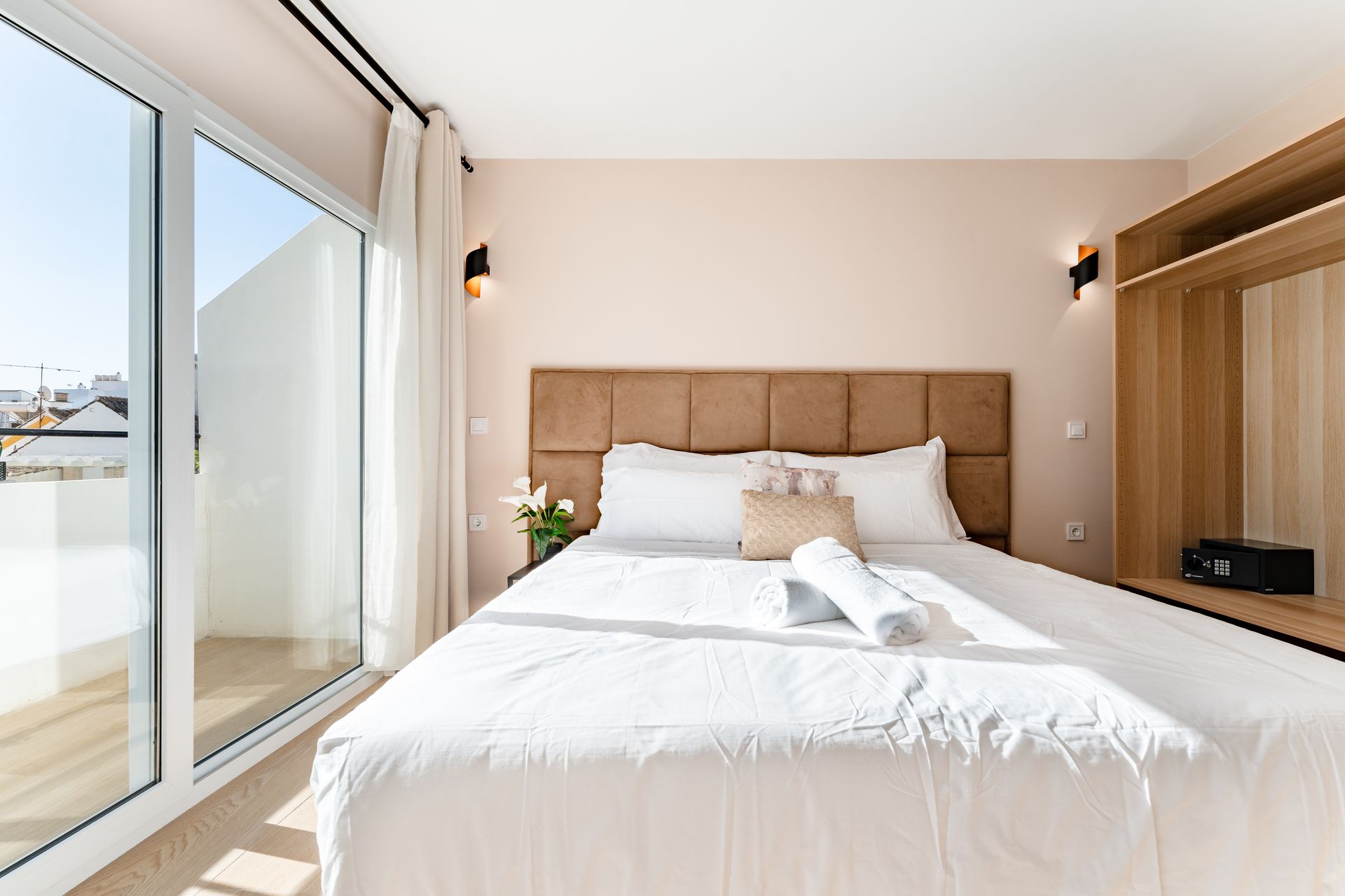 Dormitorio con cama grande, balcón y armario. Paredes rosa pálido y ropa de cama blanca.