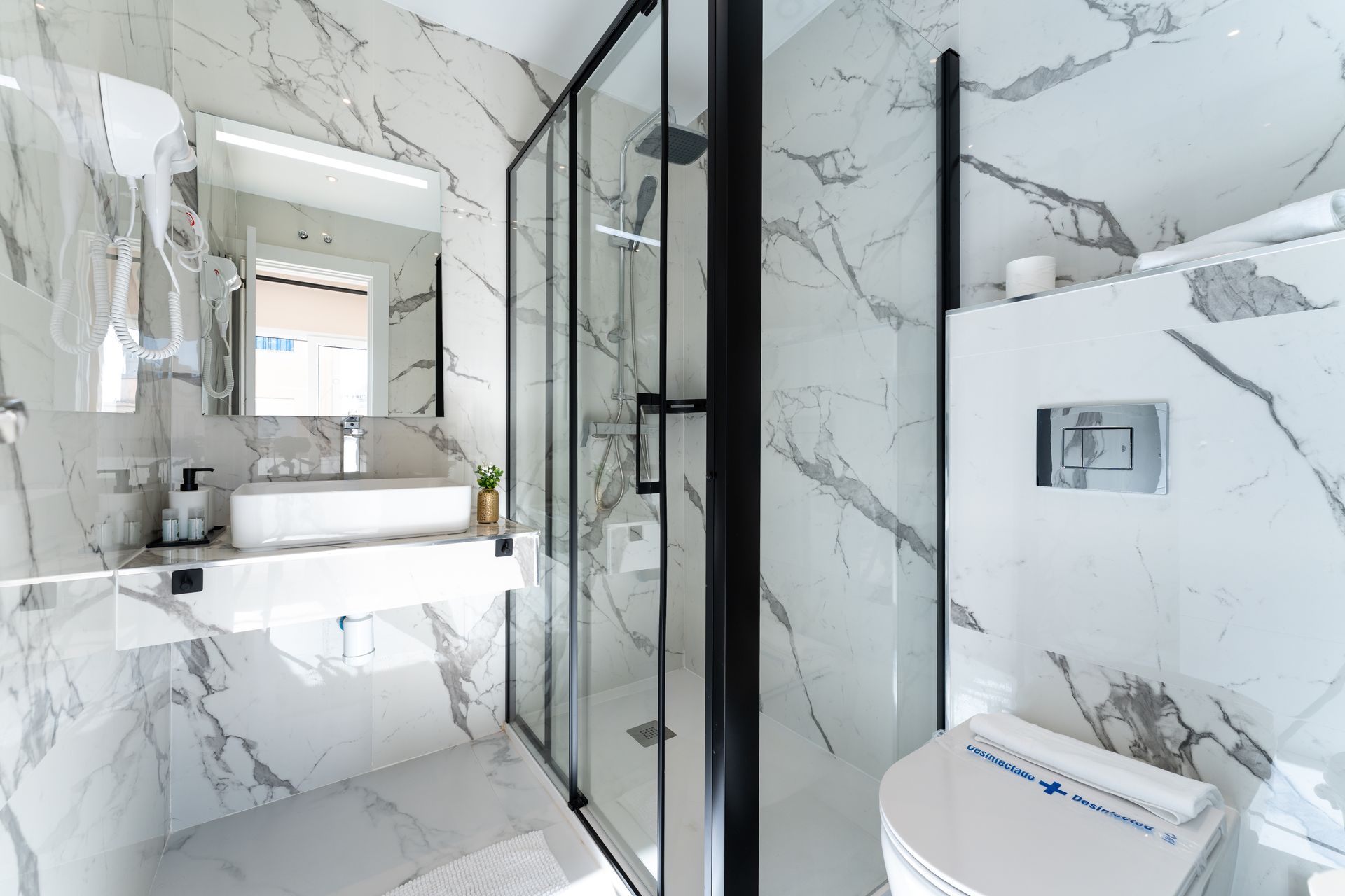 Baño moderno con paredes de mármol, ducha de cristal y lavabo suspendido.