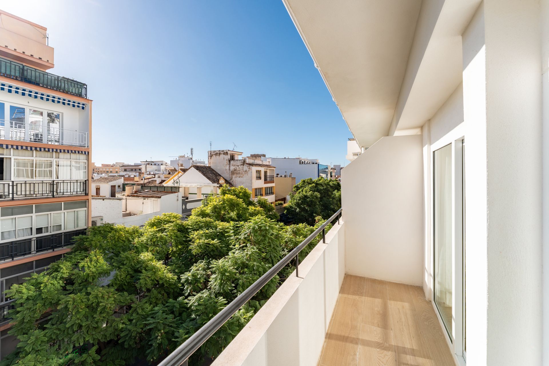 Vista desde el balcón de edificios y árboles bajo un cielo azul despejado.