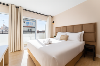 Dormitorio con cama king size, ventana grande, cabecero beige y cortinas color crema.