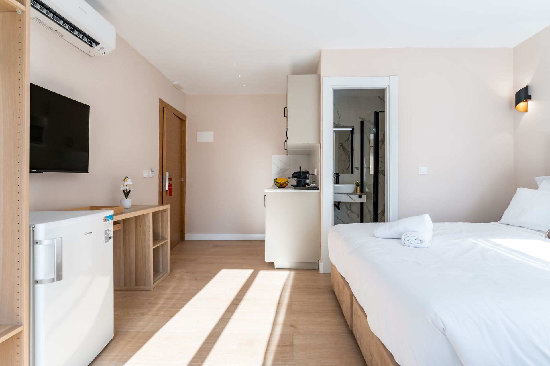 Pequeño estudio con cama, cocina americana y puerta abierta al baño. Entra mucha luz natural.