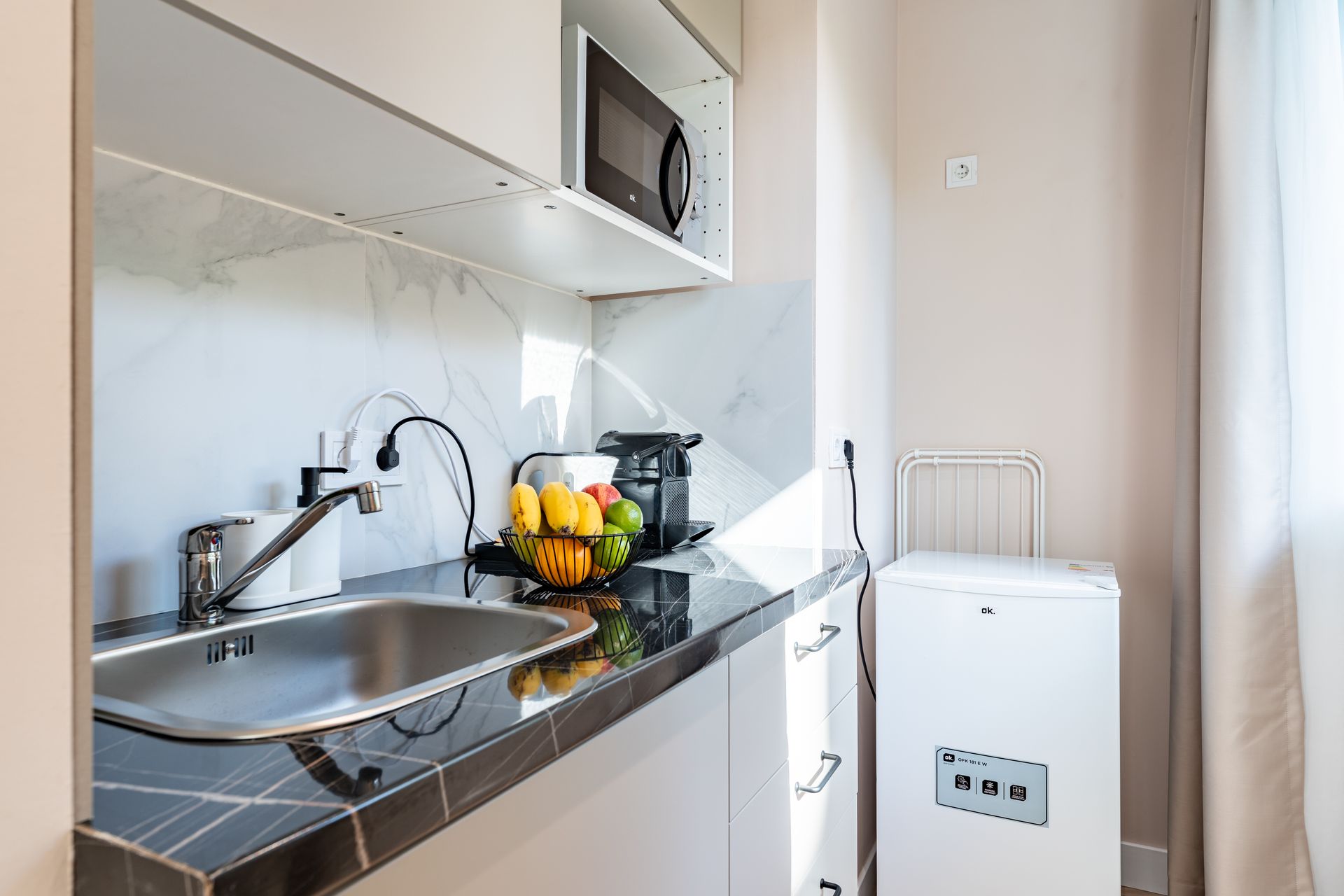 Pequeña cocina equipada con microondas, fregadero, frutero y lavadora.