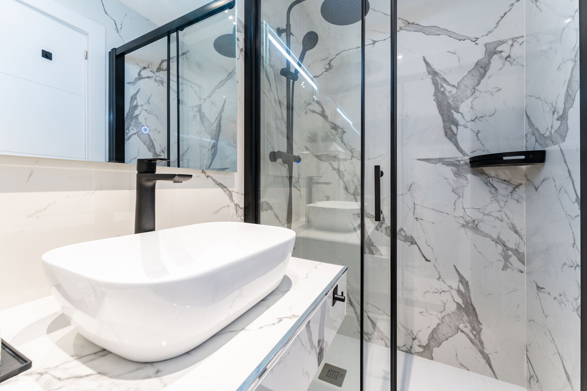 Baño moderno con paredes de mármol, lavabo sobre encimera blanco y ducha de cristal.