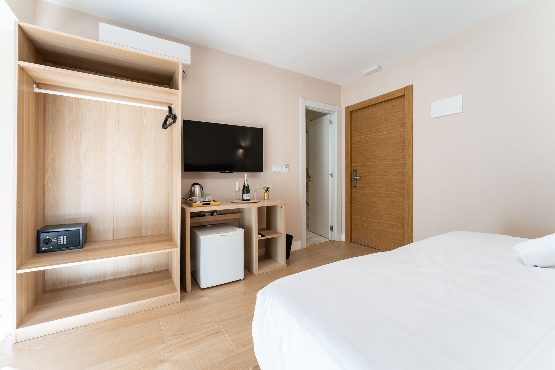 Habitación de hotel con cama, armario, TV, minibar y puerta cerrada.