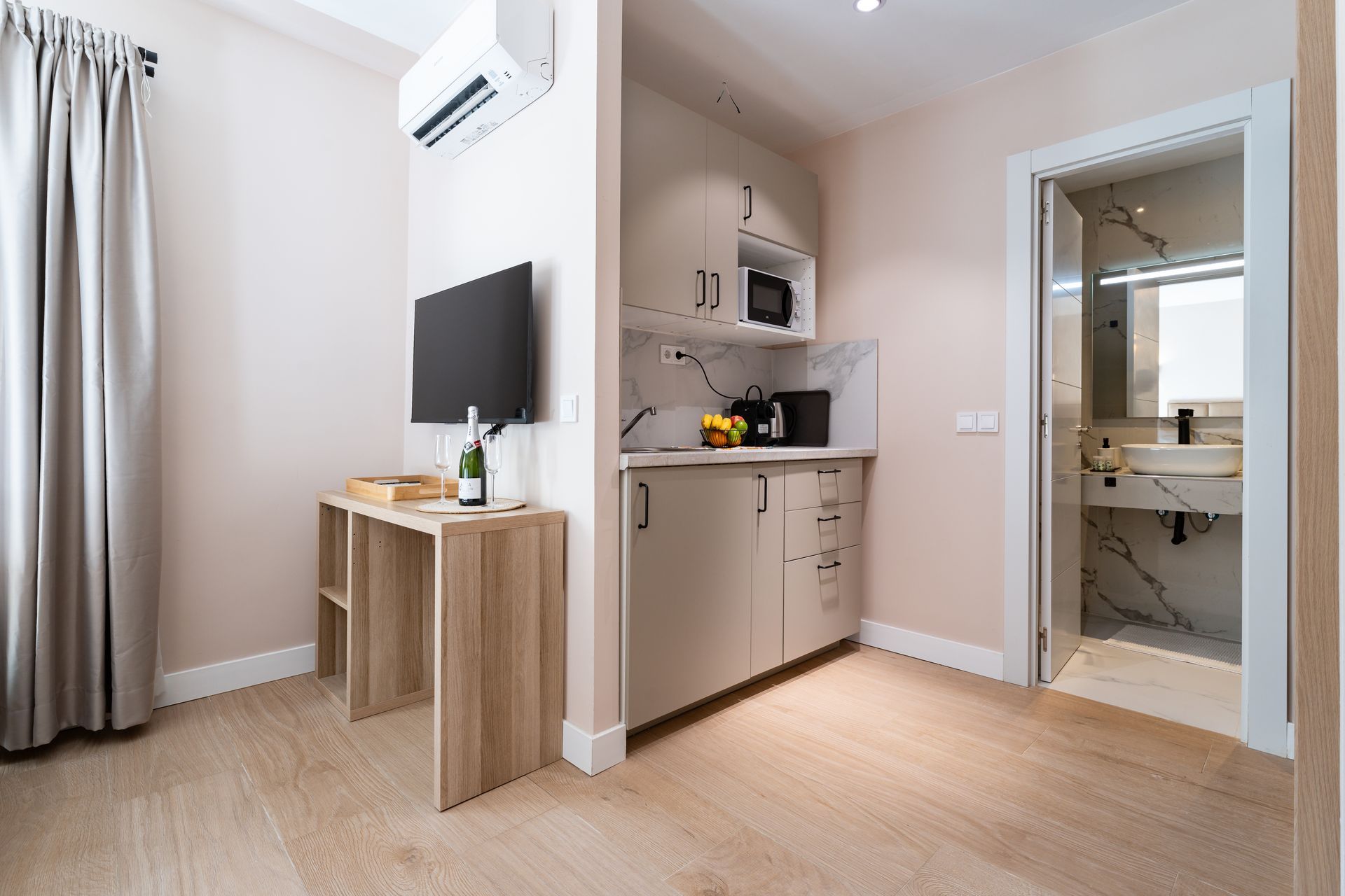 Interior de un pequeño apartamento: cocina americana, escritorio con TV y entrada al baño.