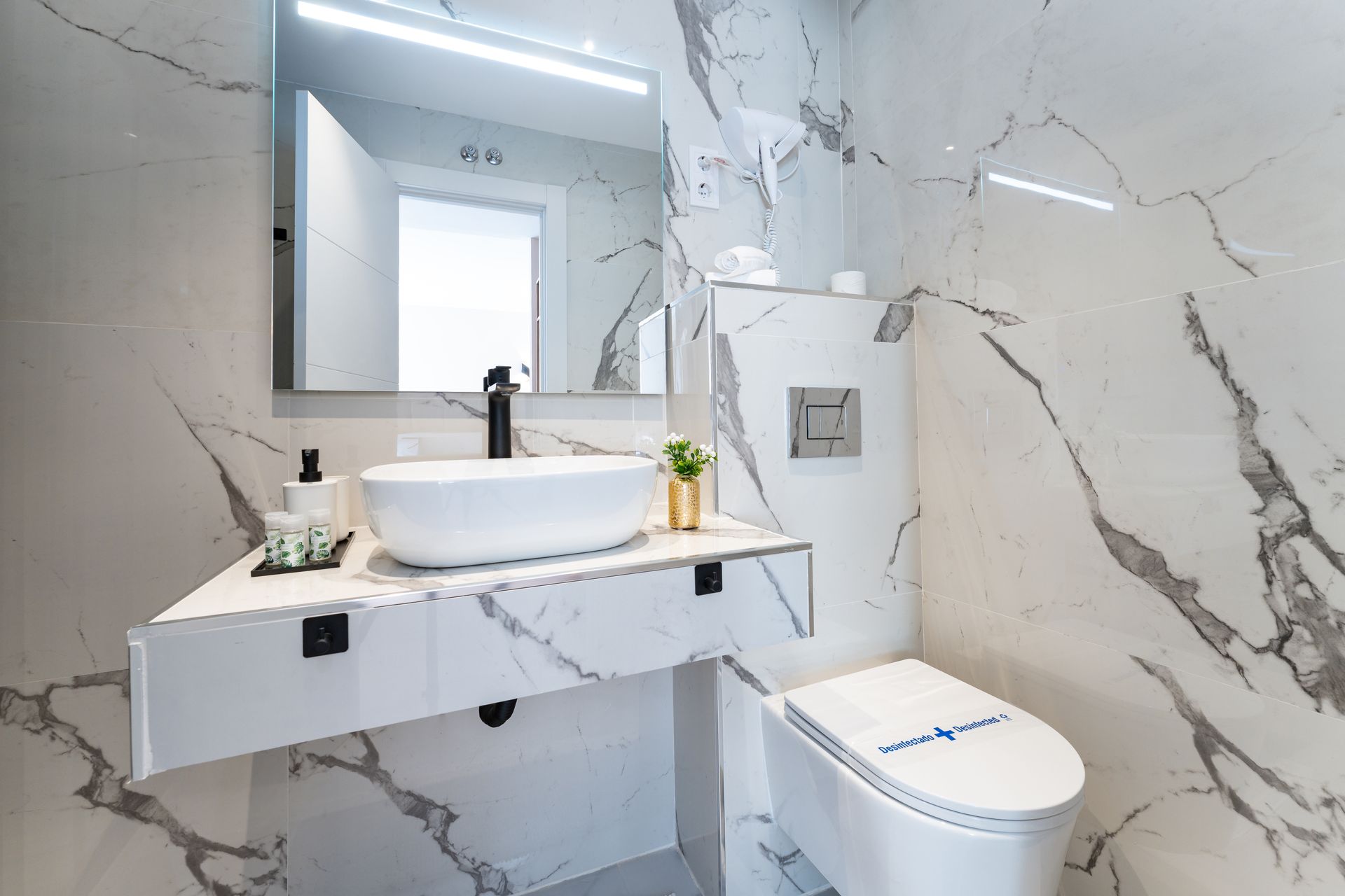 Baño moderno con paredes de mármol, lavabo blanco e inodoro.