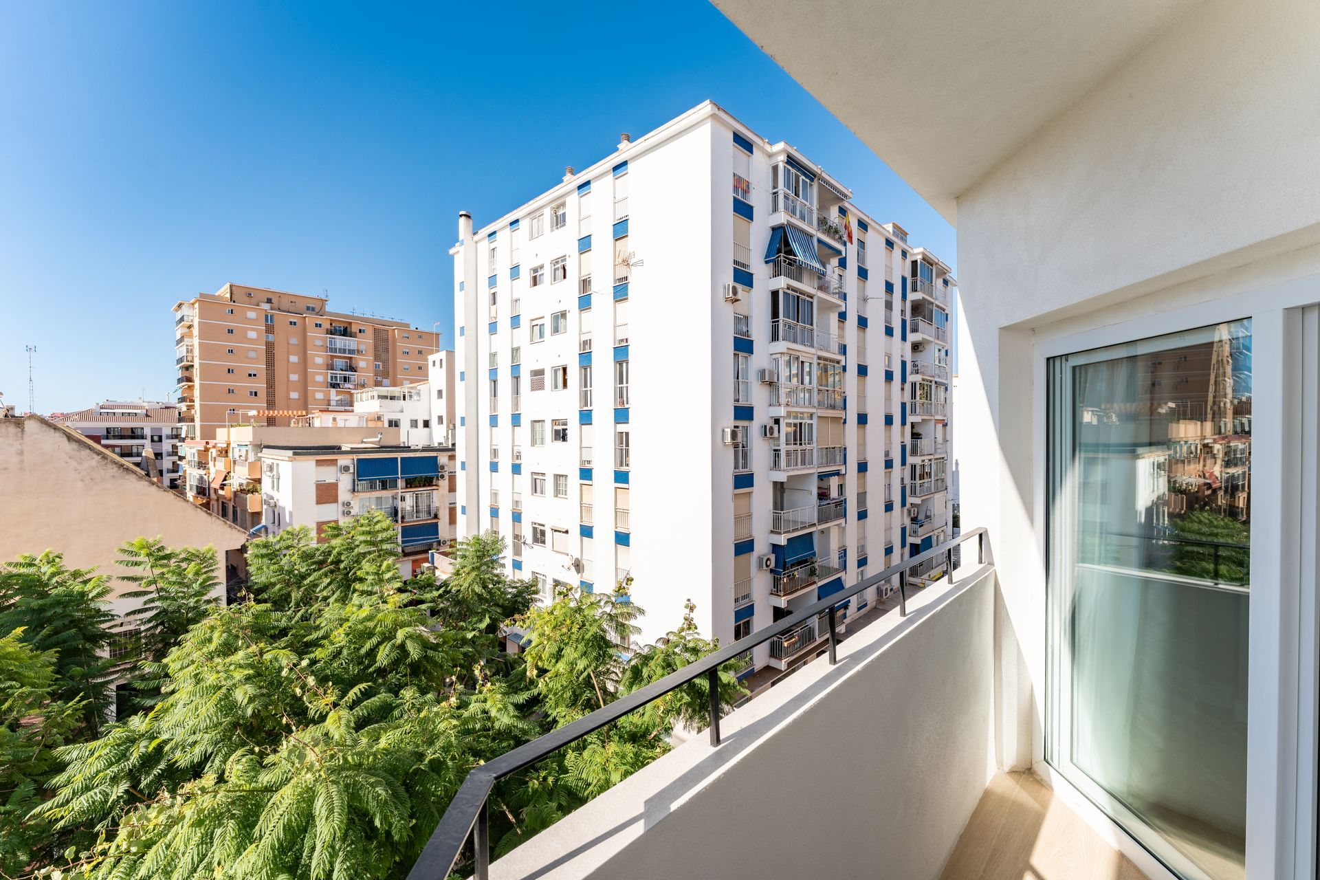 Vista desde un balcón de altos edificios blancos y azules y árboles verdes en un día soleado.