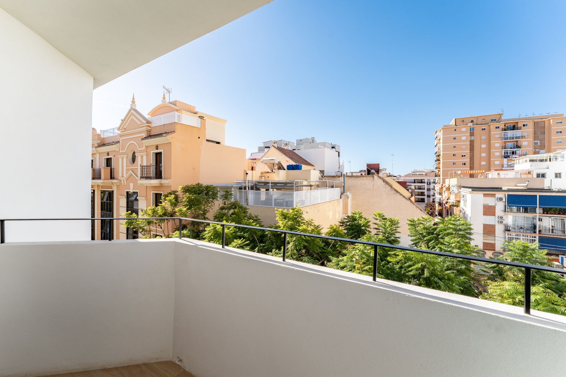 Vista desde el balcón de edificios y árboles bajo un cielo azul despejado.