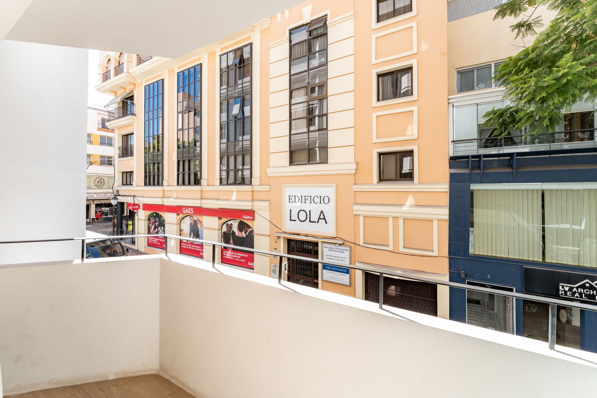 Vista desde el balcón a una calle de la ciudad con tiendas y un edificio con el letrero 