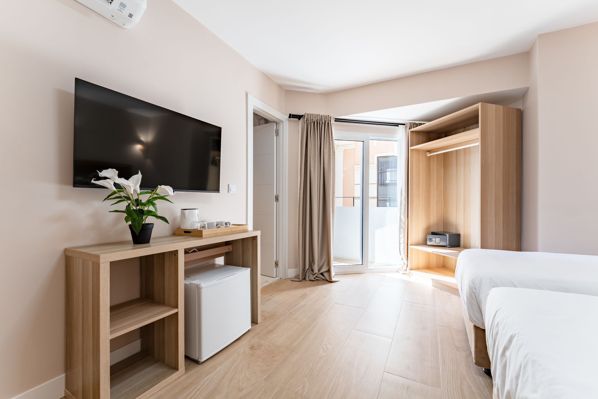 Habitación de hotel con dos camas, TV, balcón, muebles de madera y minibar.