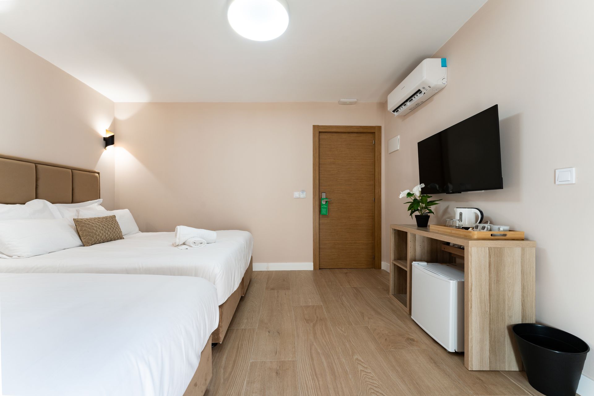 Habitación de hotel con dos camas, TV, mininevera, suelo de madera y puerta.