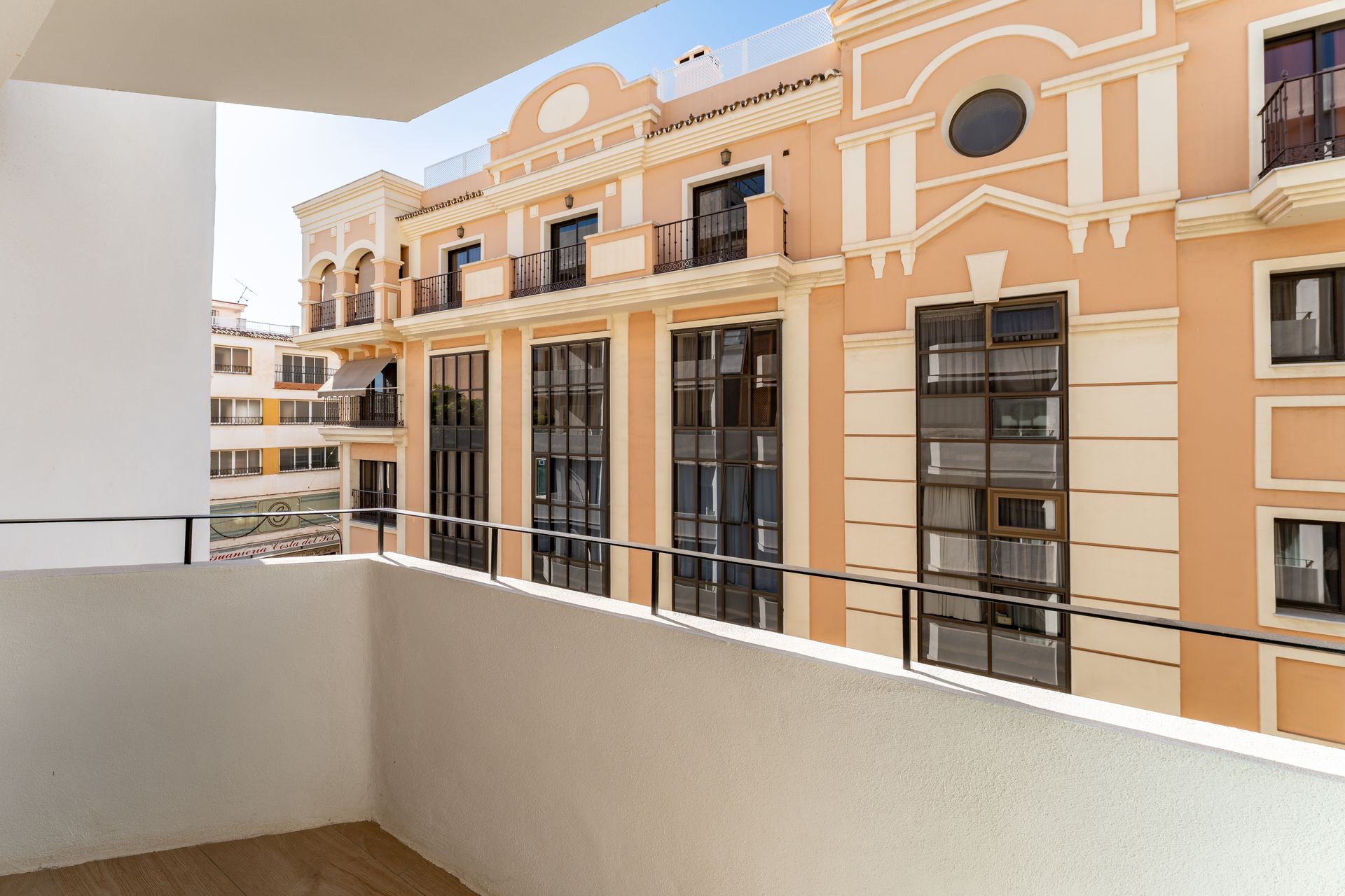 Vista desde el balcón de un edificio con fachada ornamentada, ventanas negras y cielo azul.