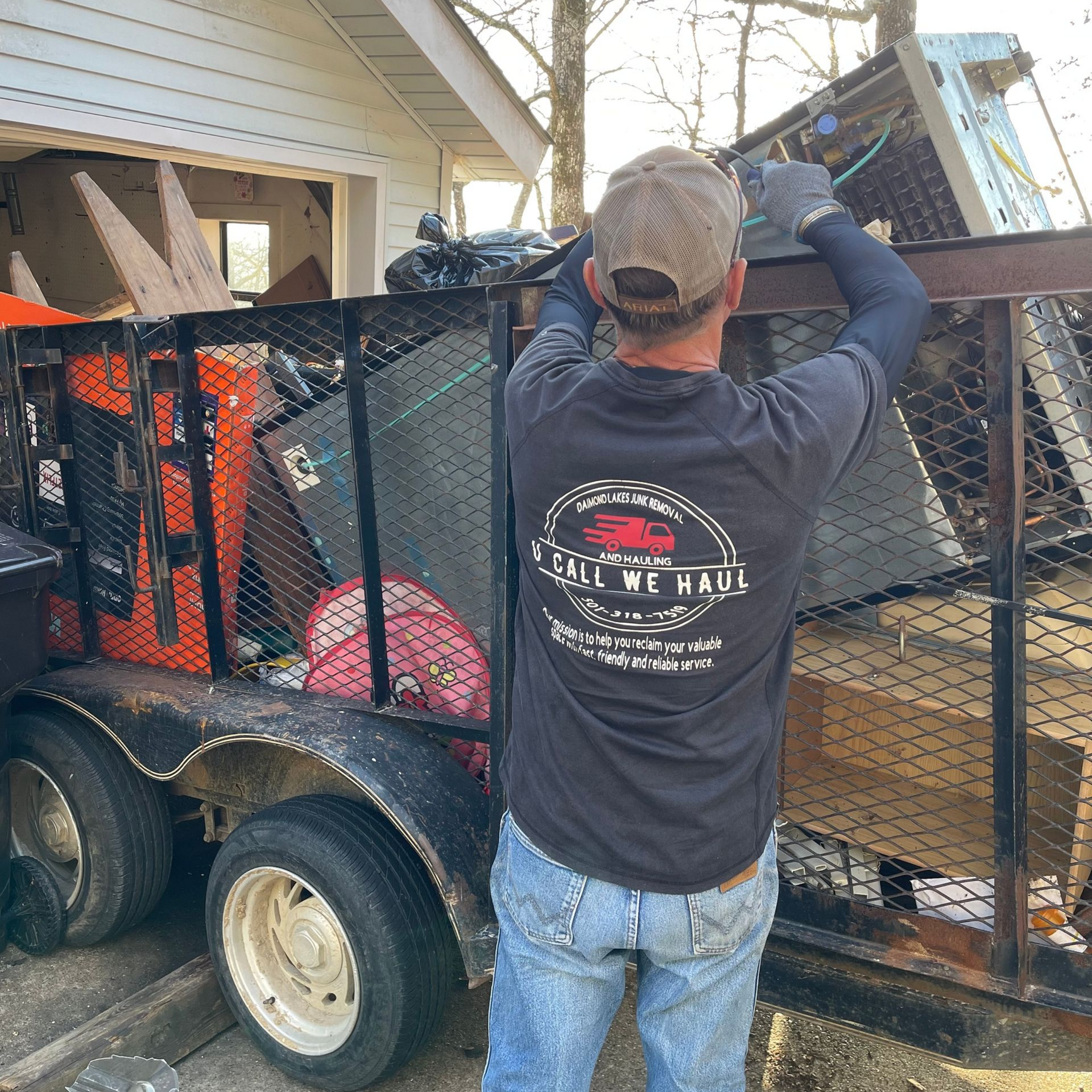 Man loading a trailer with junk, wearing a cap and a shirt that reads