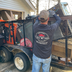 Man loading a trailer with junk, wearing a cap and a shirt that reads 