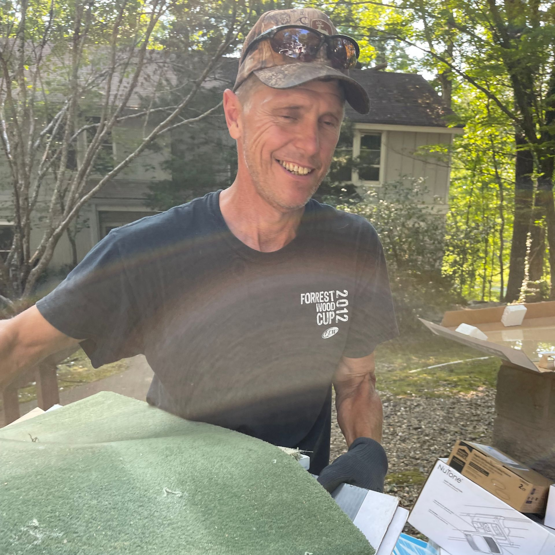 Man in camouflage hat smiles while sorting trash outdoors.