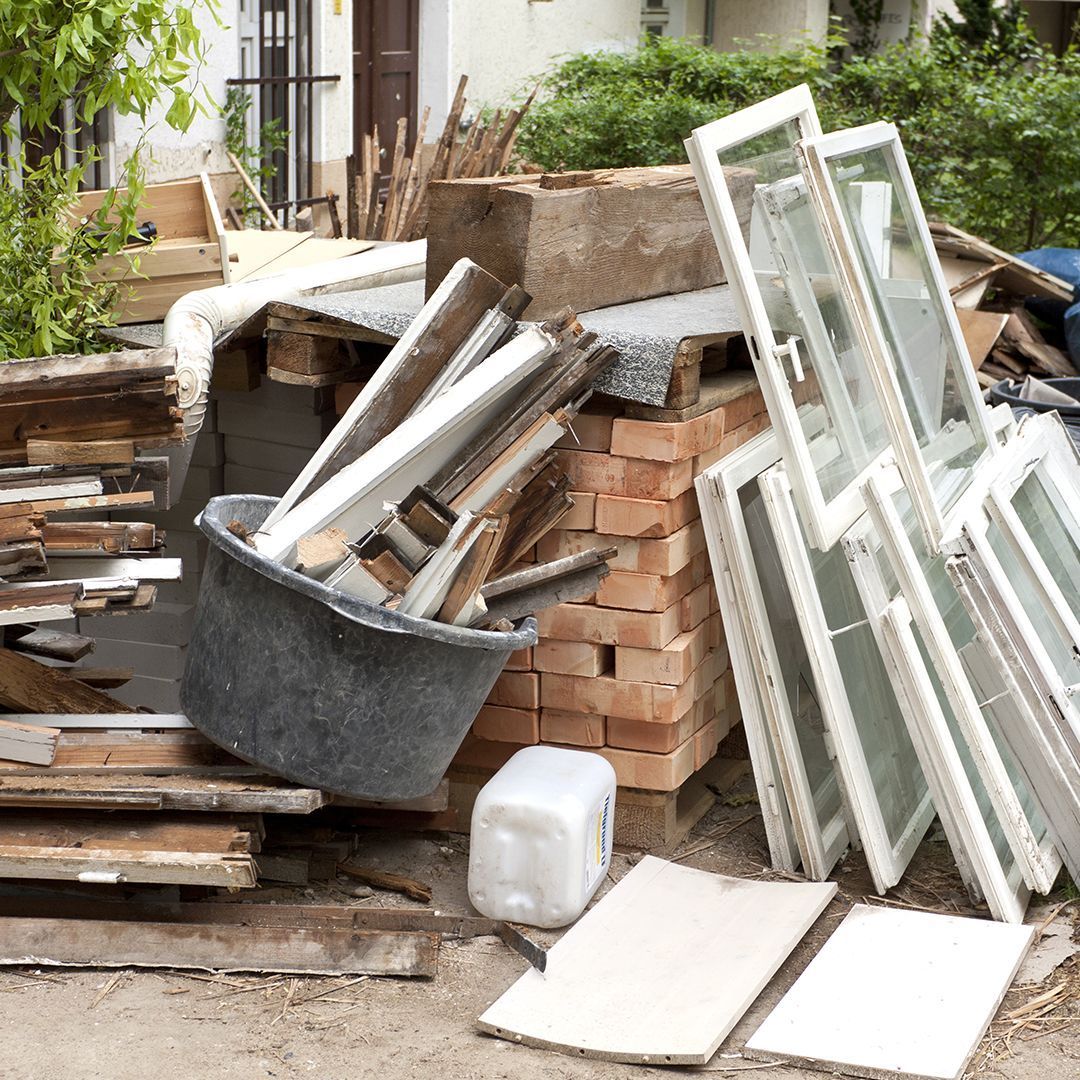 Pile of construction debris: windows, wood, bricks, and a bin in front of a building.