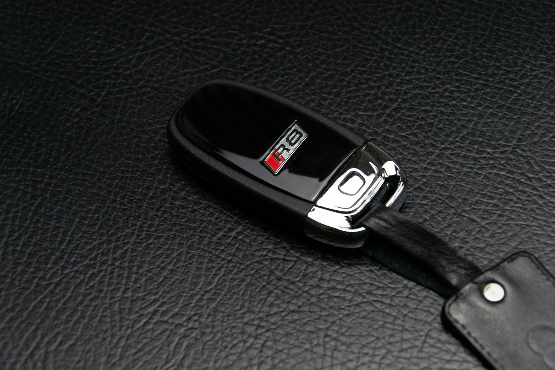 AutoPage & Glass | Milwaukee | Auto Glass Replace Black Audi R8 car key on a black leather surface.