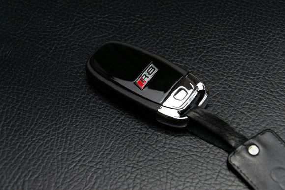Black Audi R8 car key on a black leather surface.