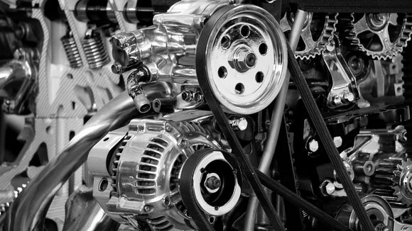 Black and white close-up of a shiny car engine, showing pulleys, belts, and various mechanical components.