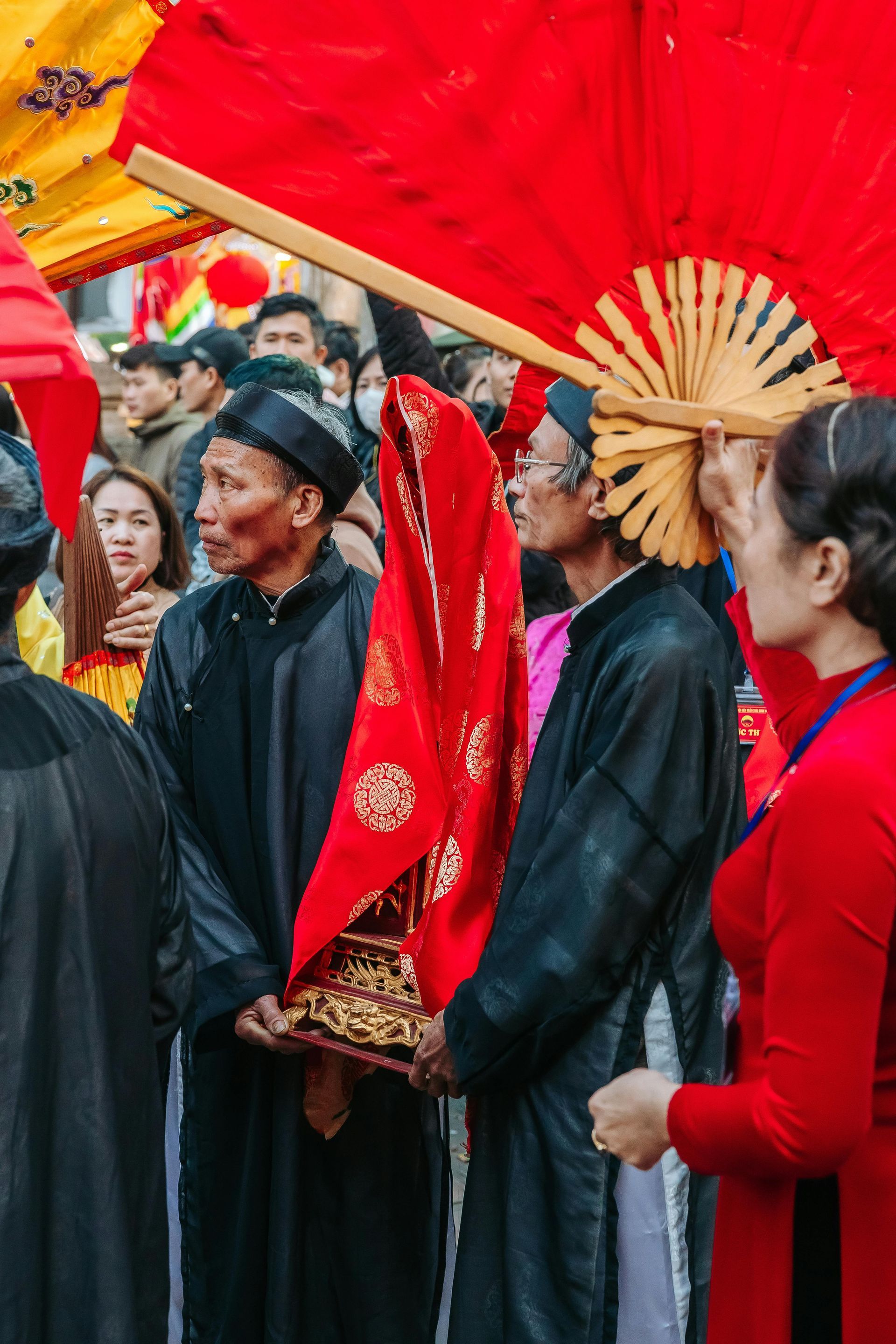 A group of people are standing in a line holding red fans.