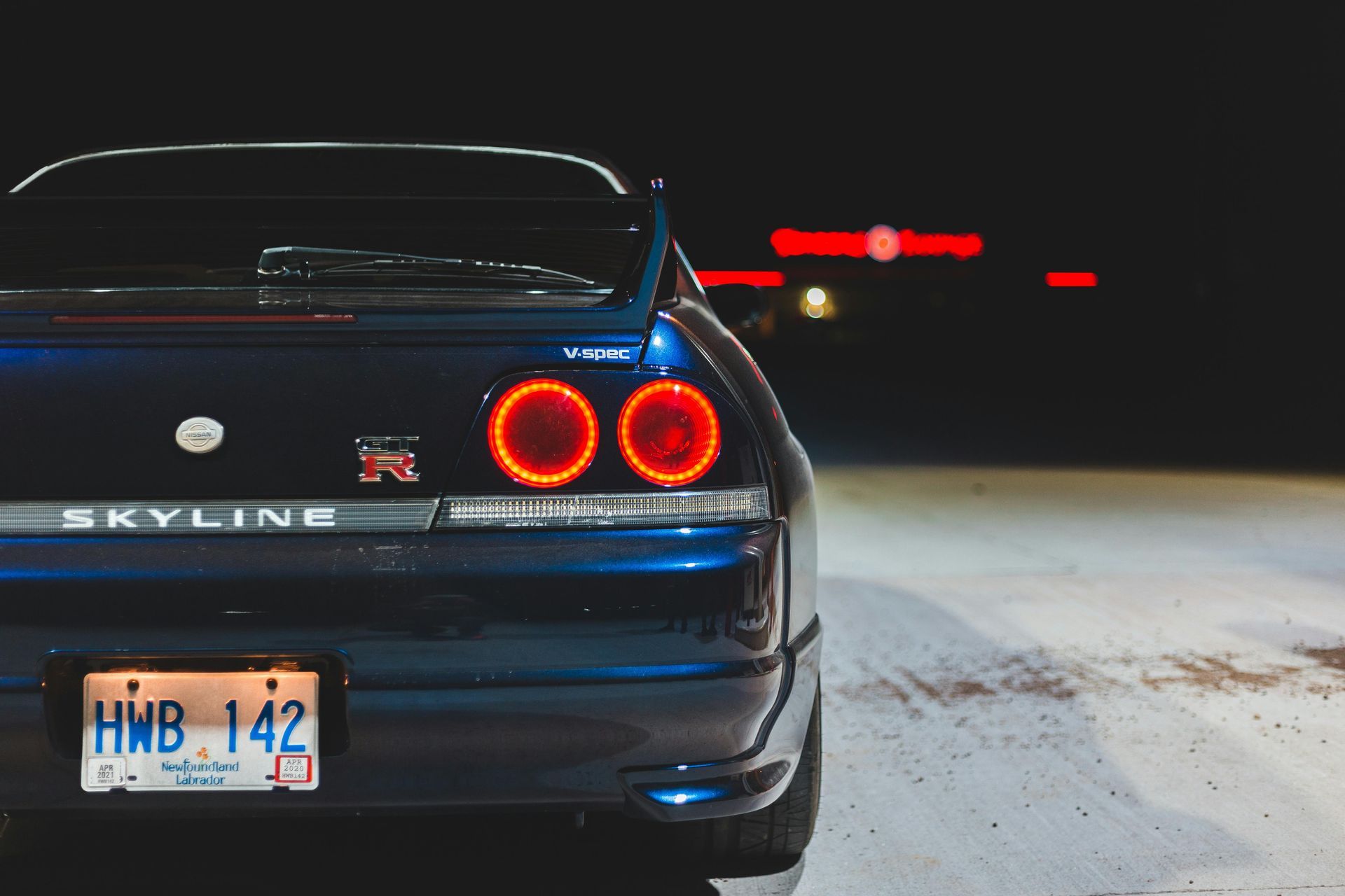 A blue nissan skyline is parked in the snow at night.