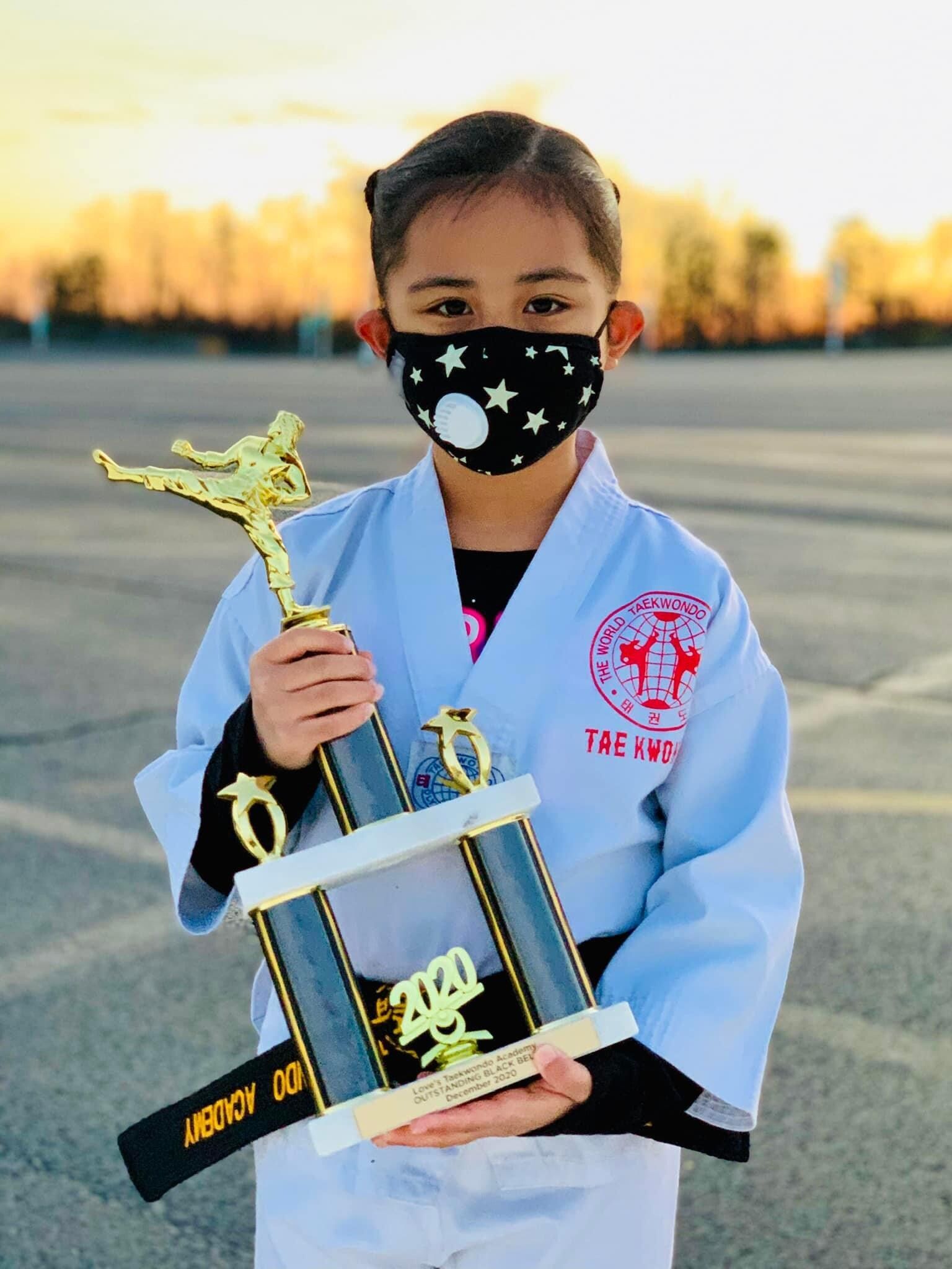 A young girl wearing a mask is holding a trophy.