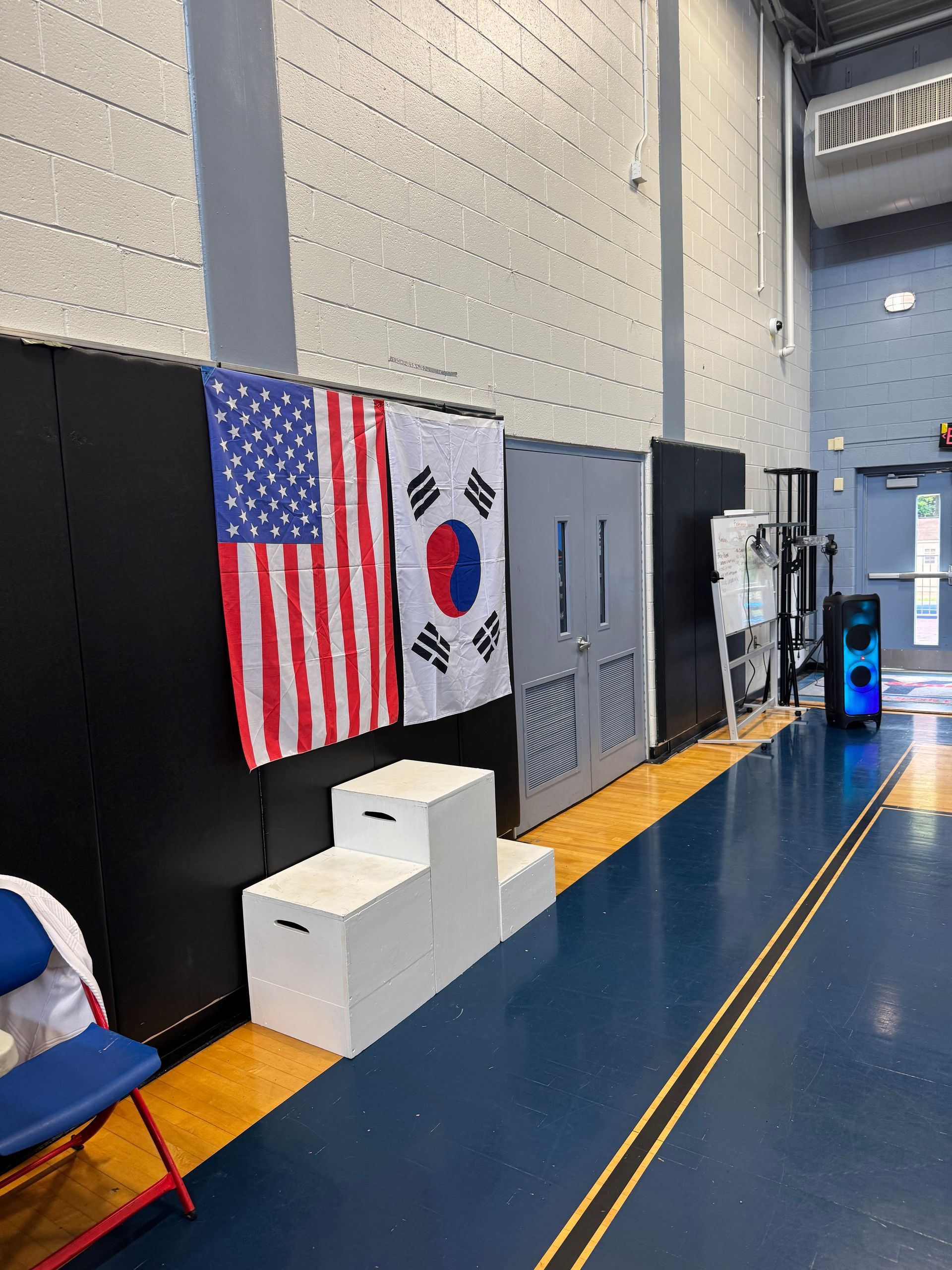 An american flag and a korean flag are hanging on a wall in a gym.