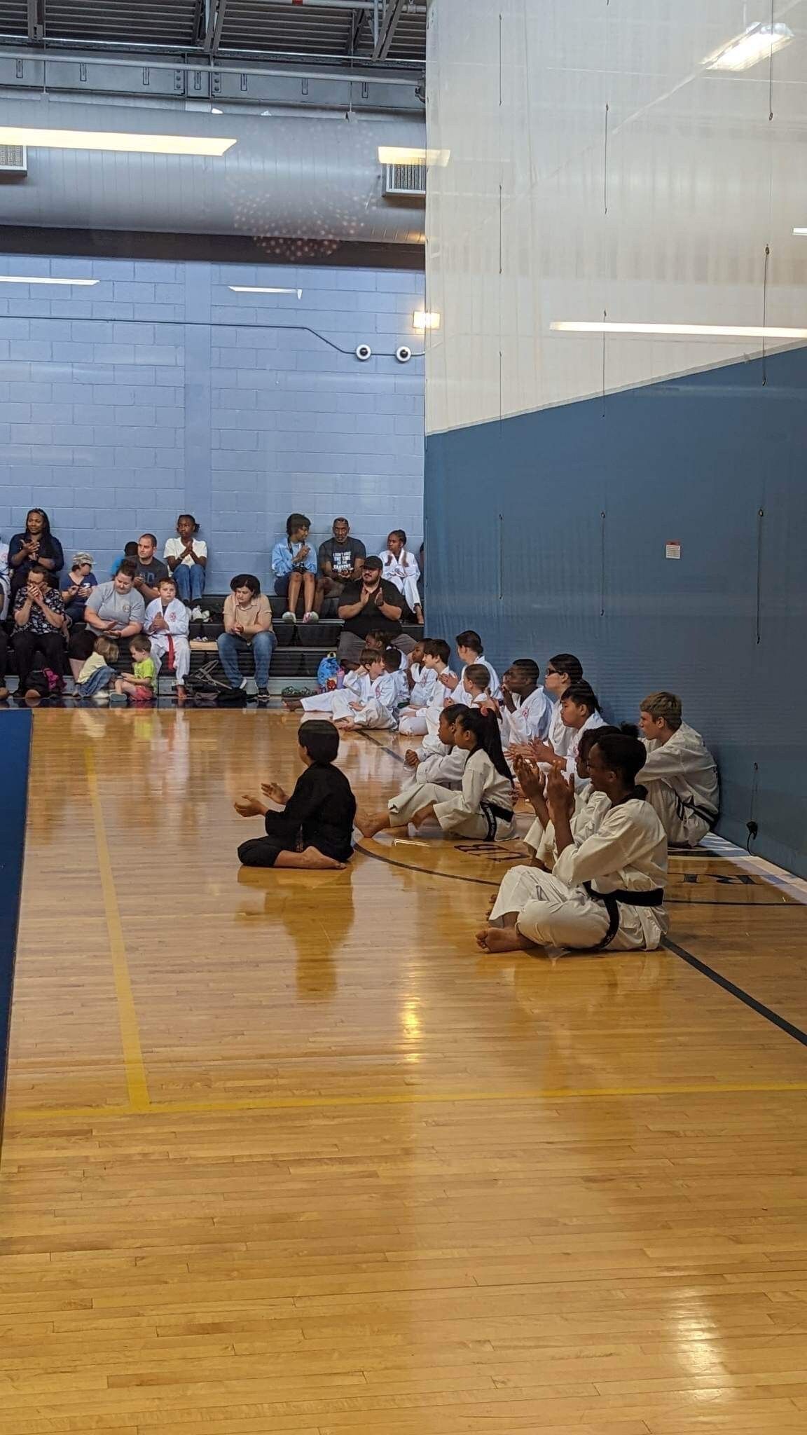 A group of people are sitting on the floor in a gym.