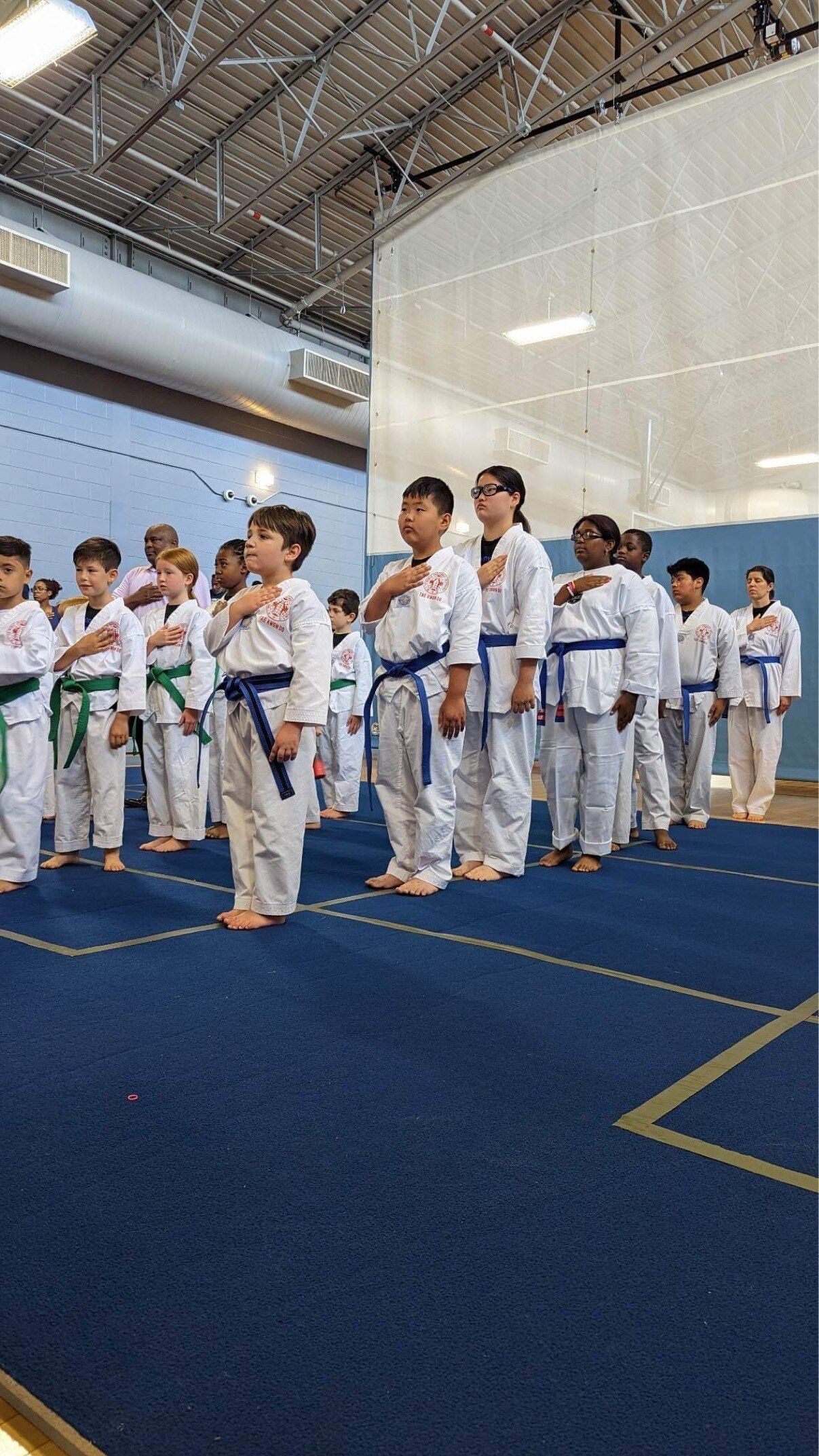 A group of children in karate uniforms are standing in a line in a gym.