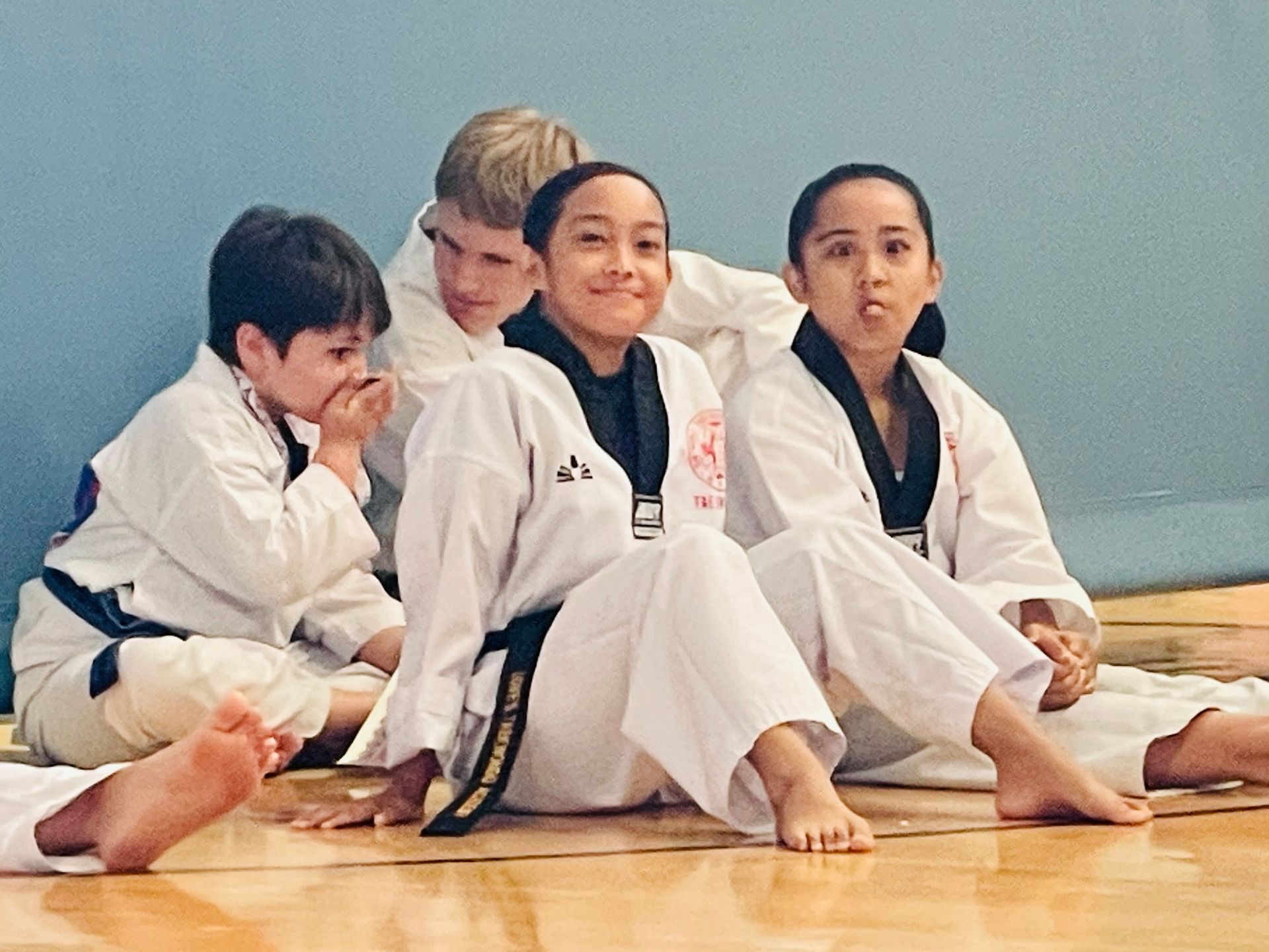 A group of kids in karate uniforms are sitting on the floor