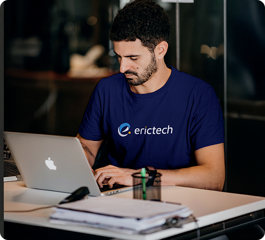 Um homem vestindo uma camisa erictech está digitando em um laptop