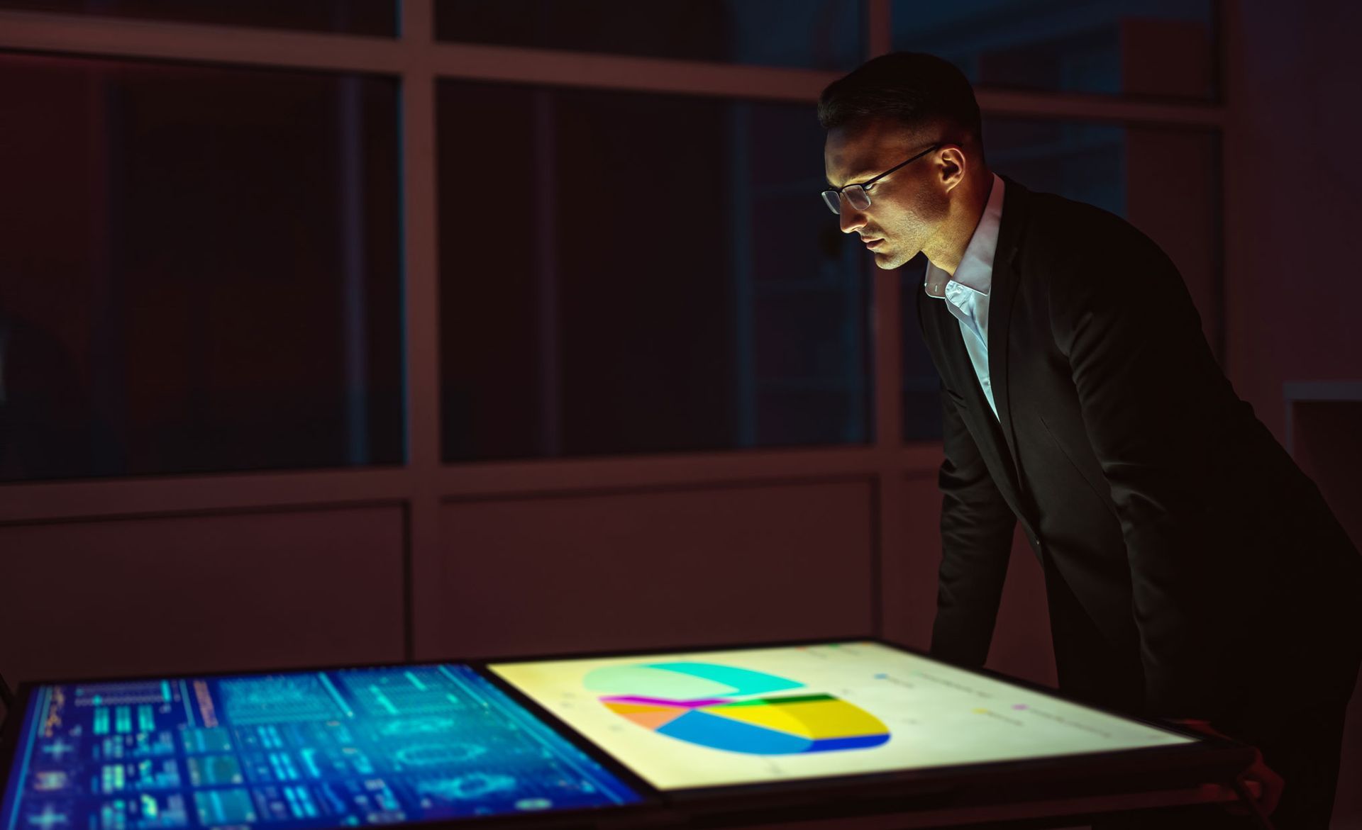 an executive in a suit is looking at a computer screen in a dark room .