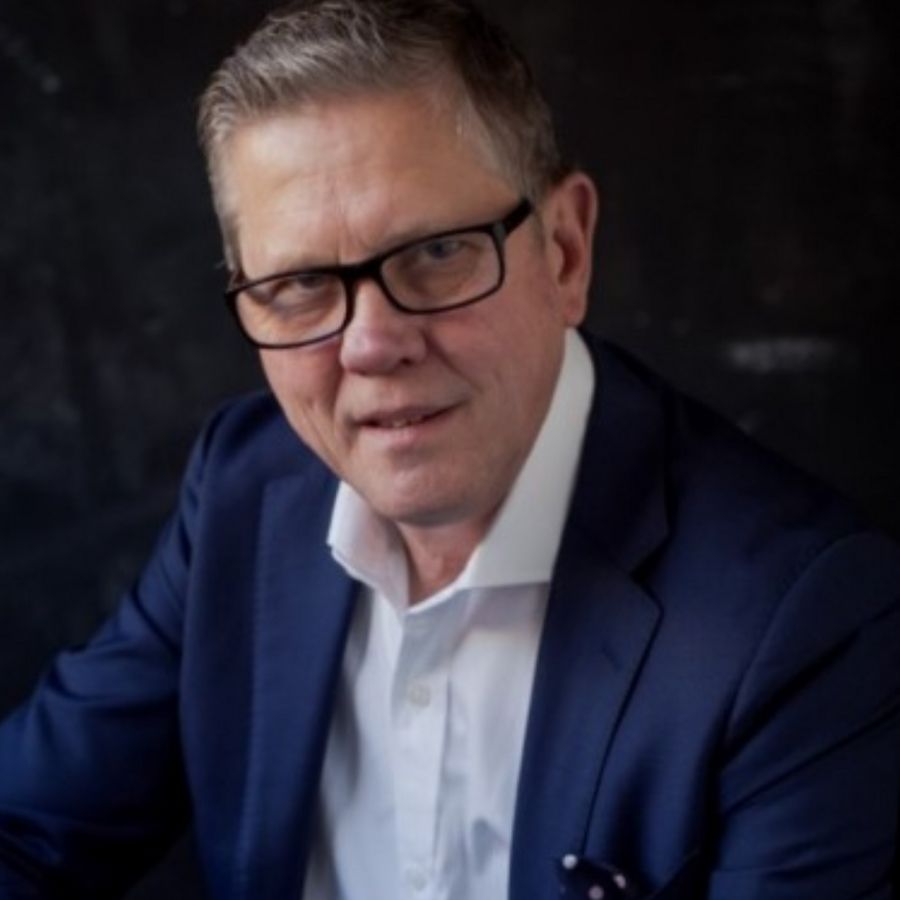 A man wearing glasses and a blue suit looks at the camera