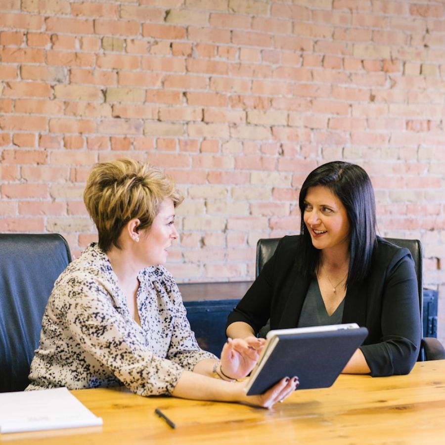 Two women are sitting at a table looking at a tablet.