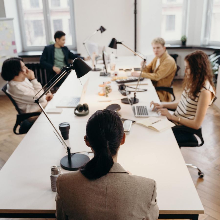 A group of people are sitting around a long table with laptops