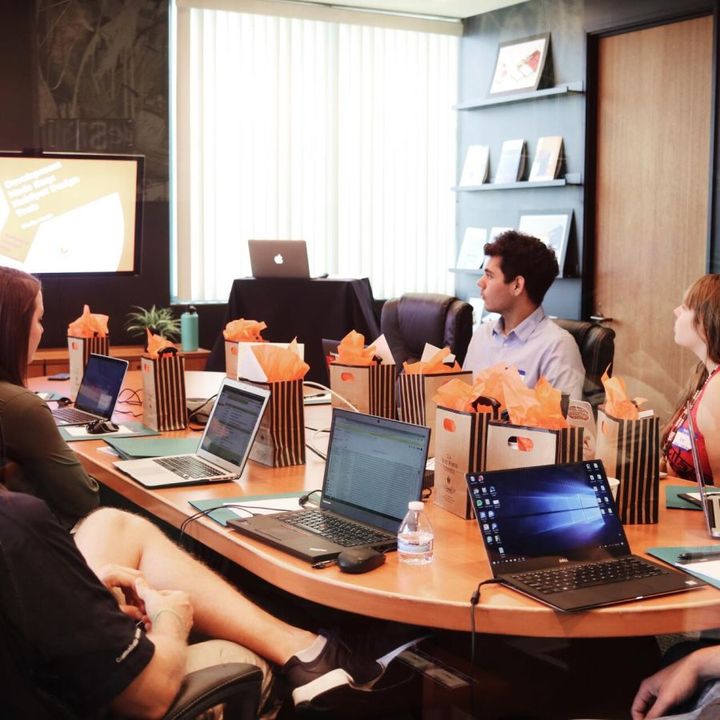 A group of people are sitting around a table with laptops