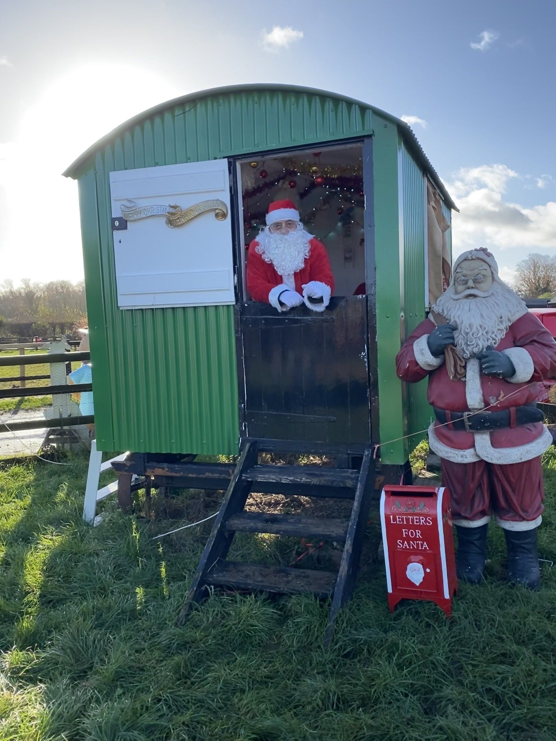 Two santa clauses are standing in front of a green shack.