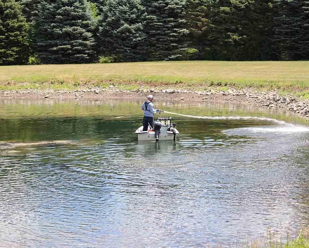 Man in waders collecting a water sample from a calm lake.
