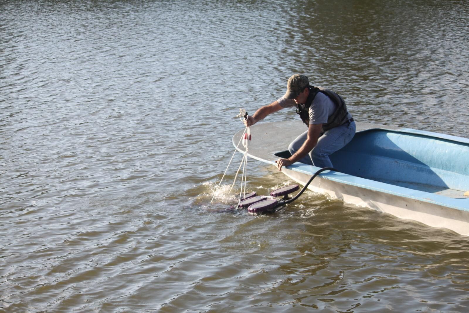Man in waders collecting a water sample from a calm lake.