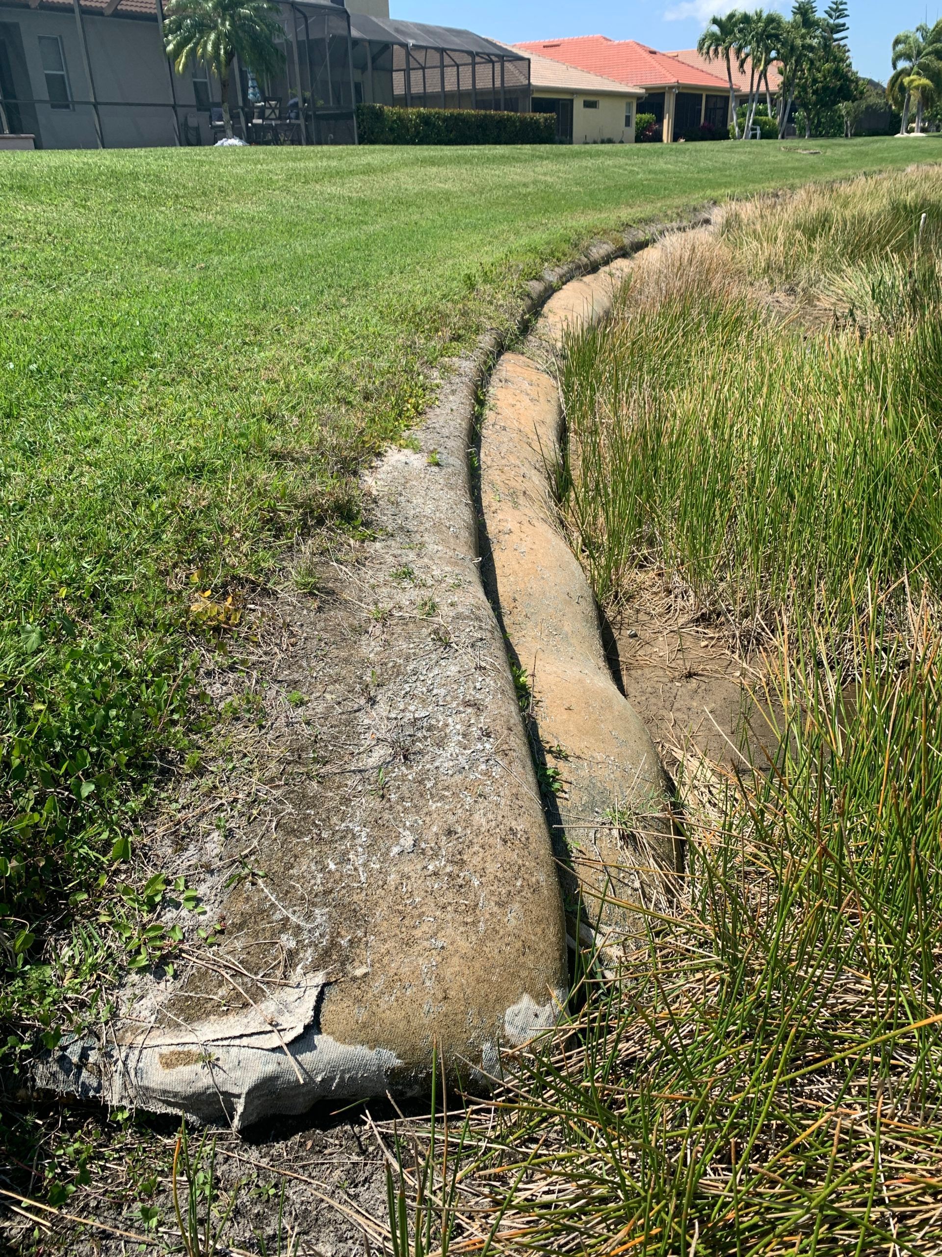 Concrete drainage ditch in grassy area near houses.
