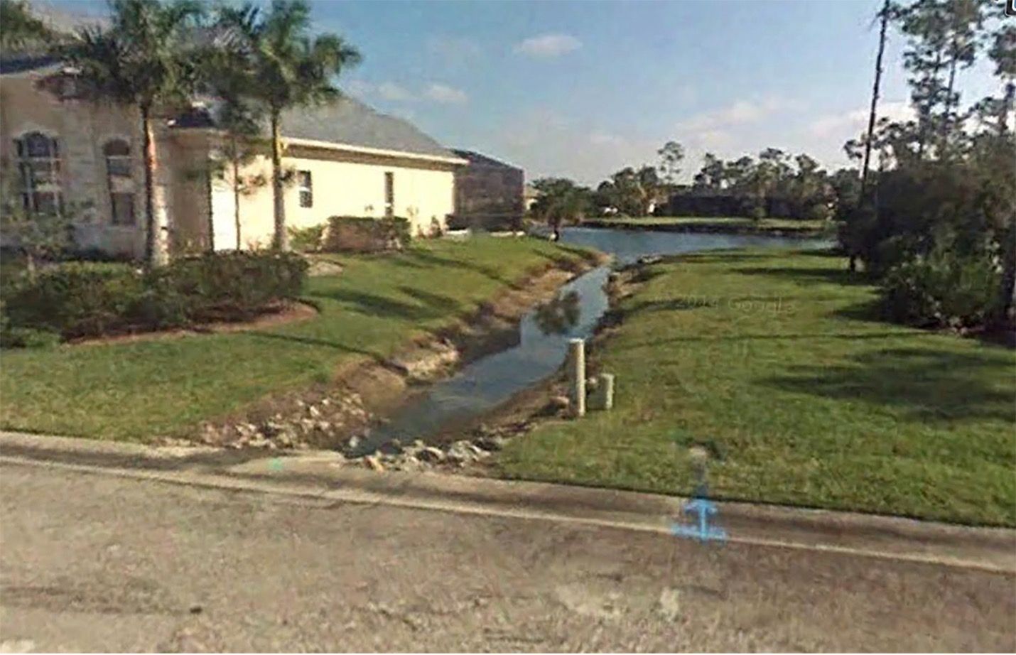 Residential area with canal and lake. Light colored house, green grass, palm trees.