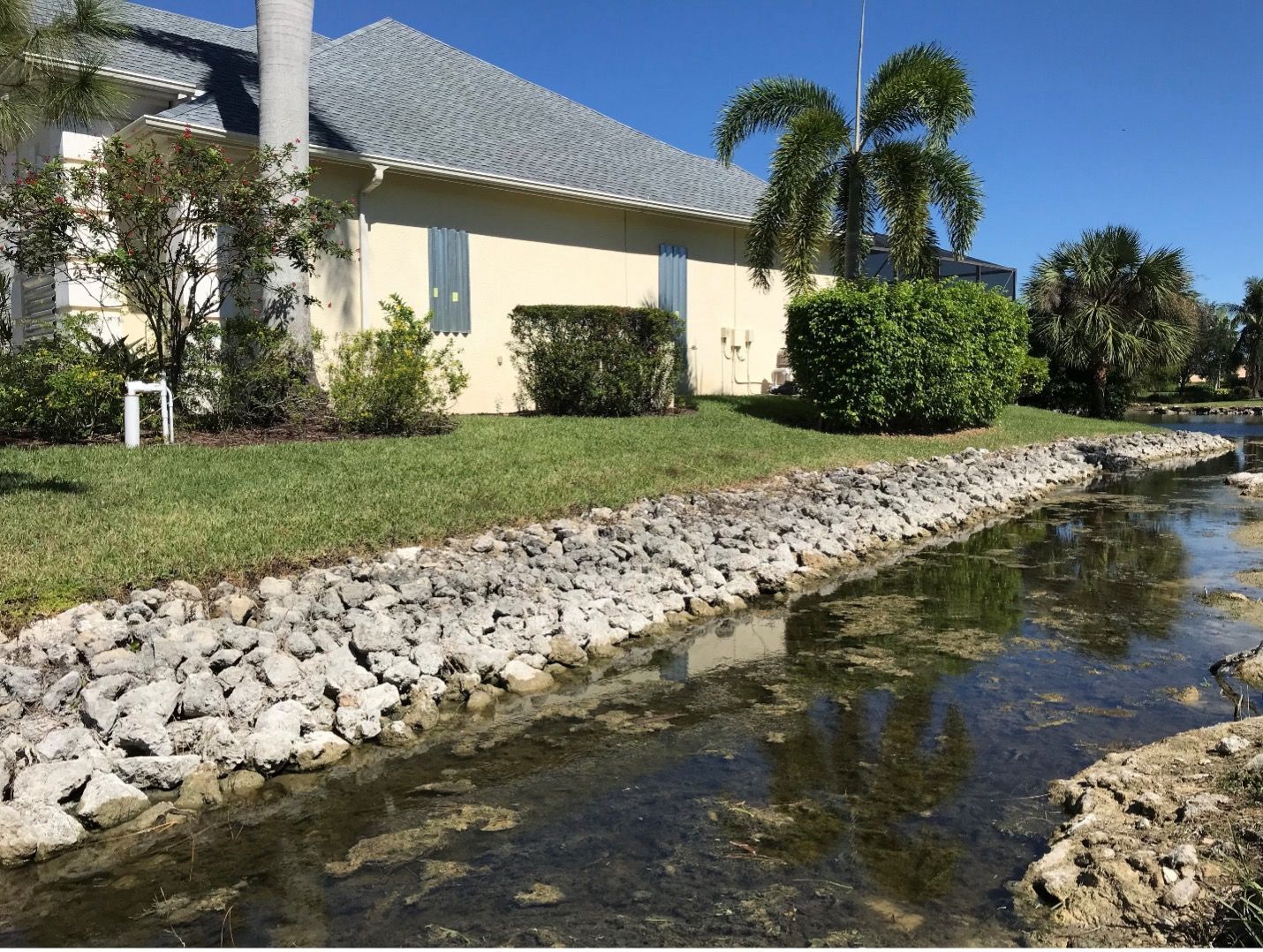 A rock-lined waterway next to a building with a blue roof, under a bright blue sky.