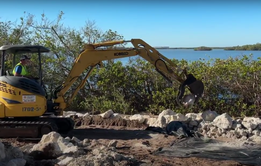 a man is driving a yellow excavator on a rocky beach .