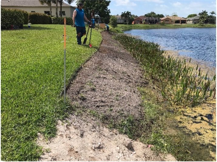 Man working on shoreline near a lake, with grass and water visible.