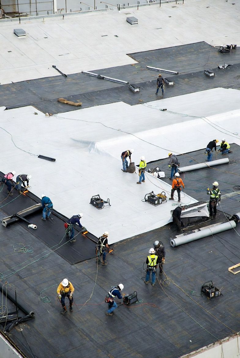 Construction workers installing roofing materials on a large, flat roof.