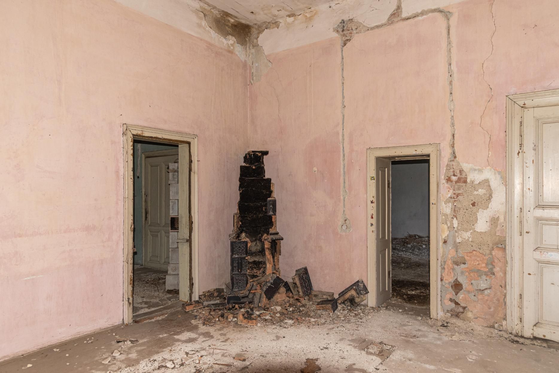 An abandoned, pink-walled room with two open doorways and a tall, precarious stack of black debris in the corner.