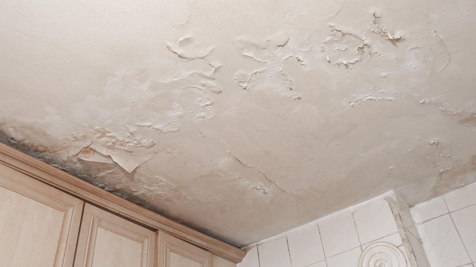 Water damage on a white kitchen ceiling, showing peeling paint.