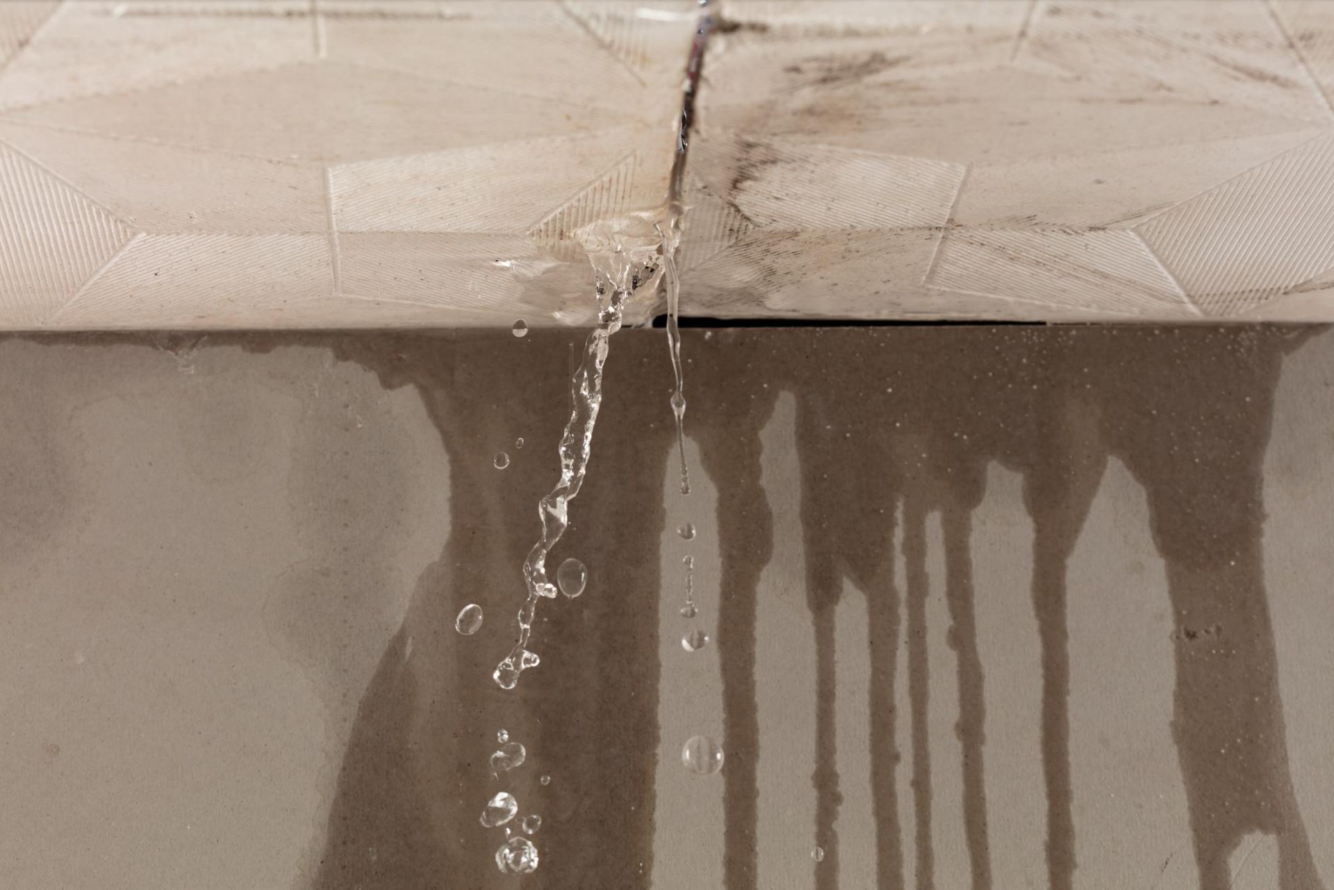 Water leaks through a crack between two light-colored tiles.